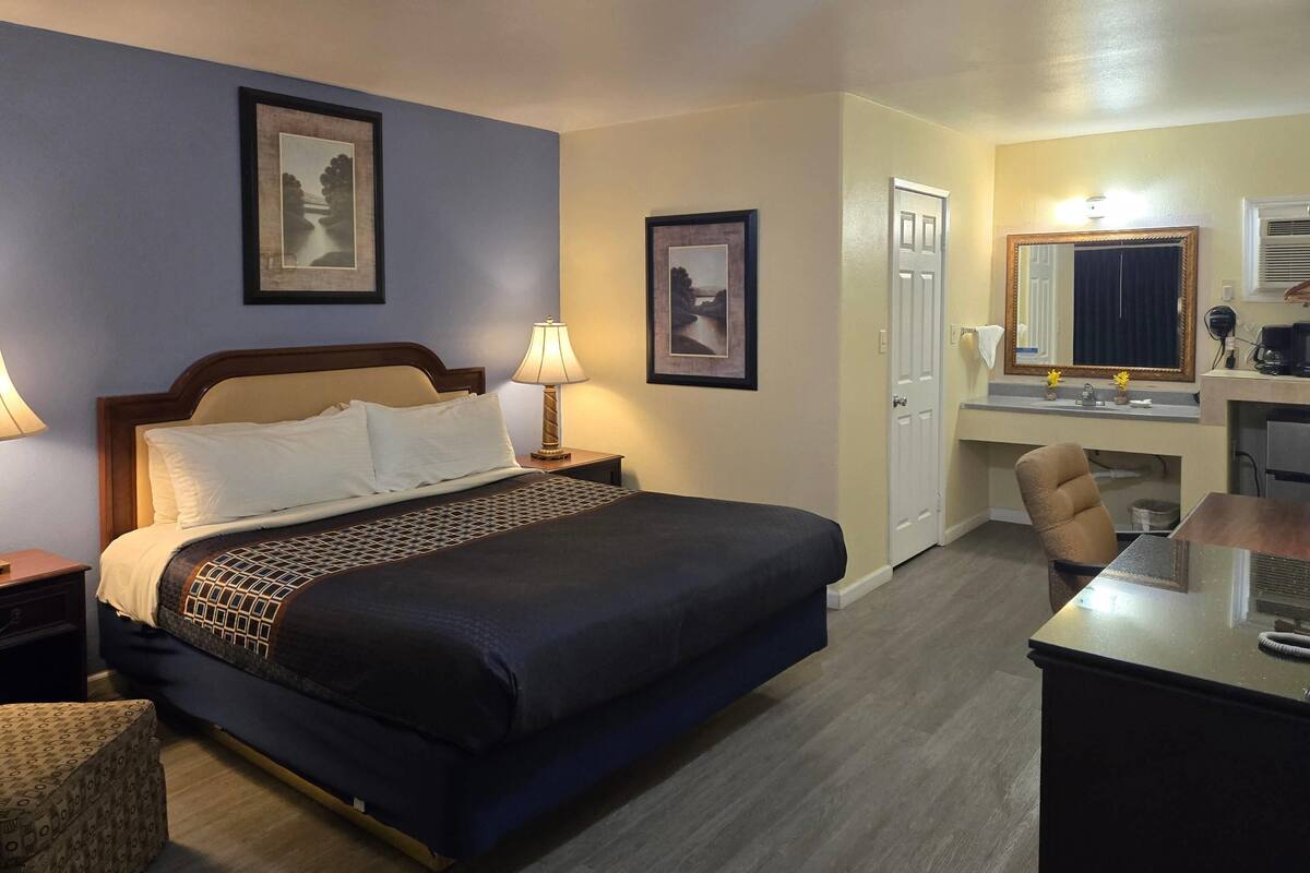 A hotel room with a bed, a desk, a chair, a lamp, and two framed pictures on the wall.