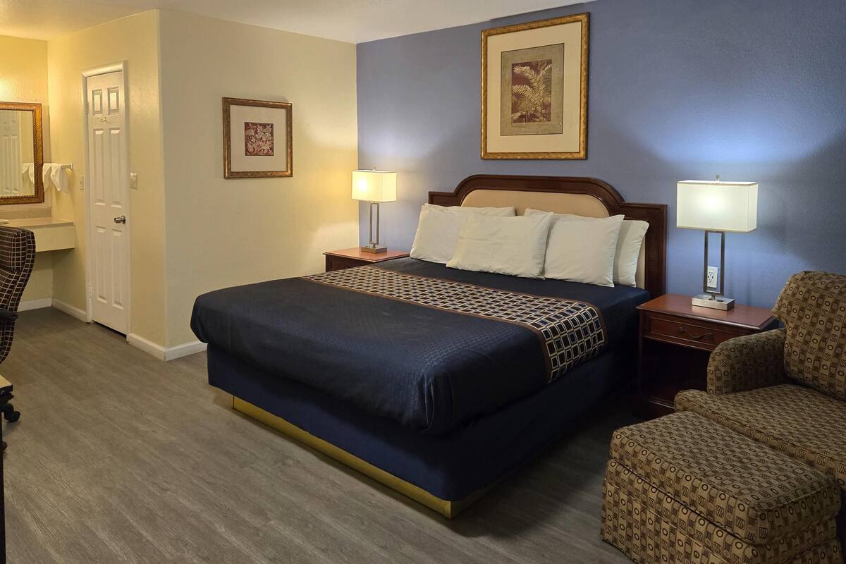 A hotel room with a large bed, two bedside tables with lamps, a chair, and a door.
