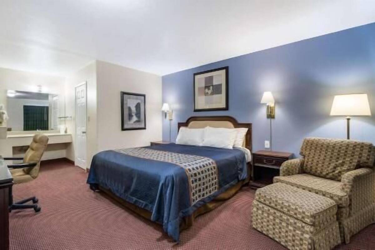 A hotel room with a bed, a desk, a chair, and a lamp.