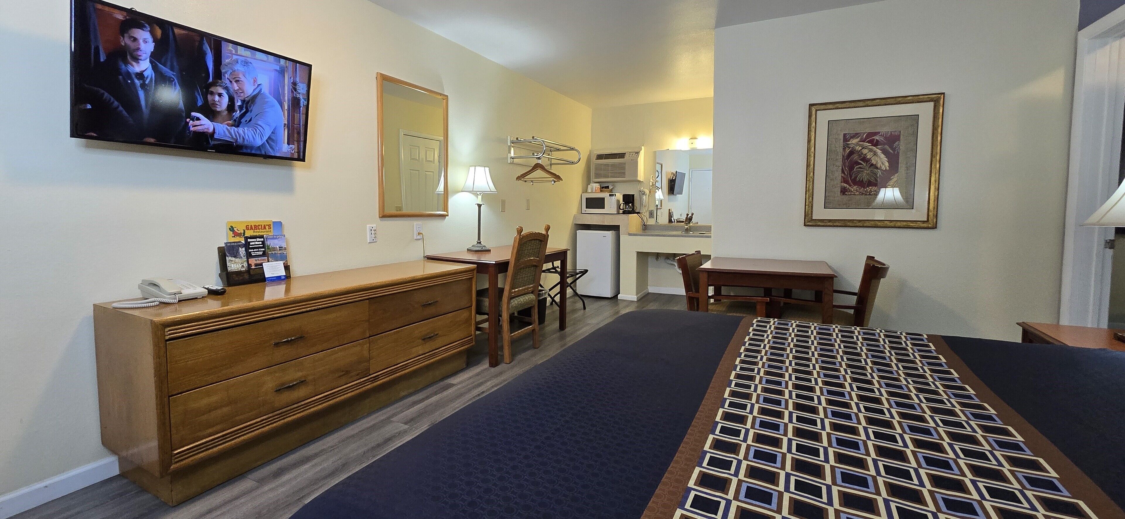 A hotel room with a bed, a dresser, a desk, a chair, a TV, a microwave, a coffee maker, and a framed picture on the wall.