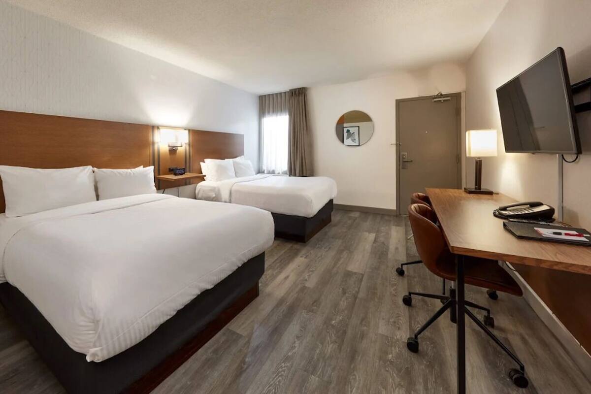 A hotel room with two beds, a desk, a chair, a TV, a lamp, and a clock on the wall.