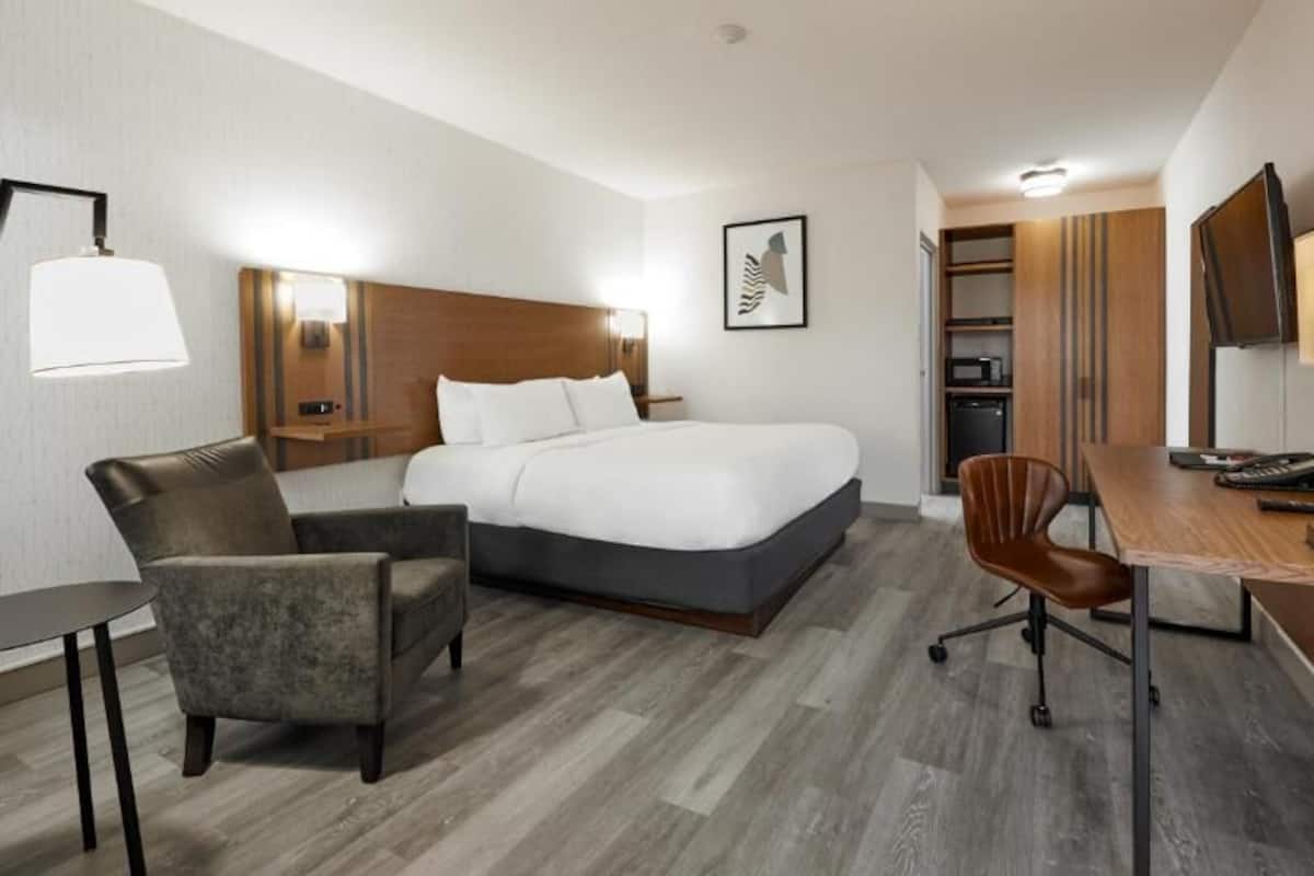 A hotel room with a bed, a desk, a chair, a lamp, and a TV.