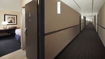 Un pasillo de hotel con una puerta que da a una habitación, un escritorio con una silla y un cuadro en la pared.