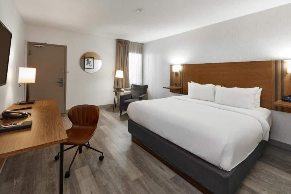 A hotel room with a bed, desk, chair, lamp, and a TV.