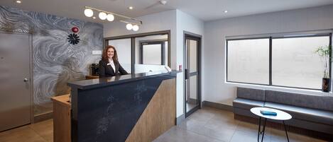A modern reception area with a marble counter, a large window with a view, a seating area, and a wall with a unique pattern.