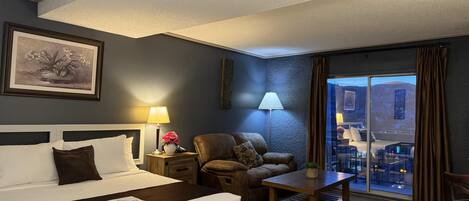 Ett hotellrum med en säng, ett skrivbord, en stol, en lampa och utsikt över omgivningarna.