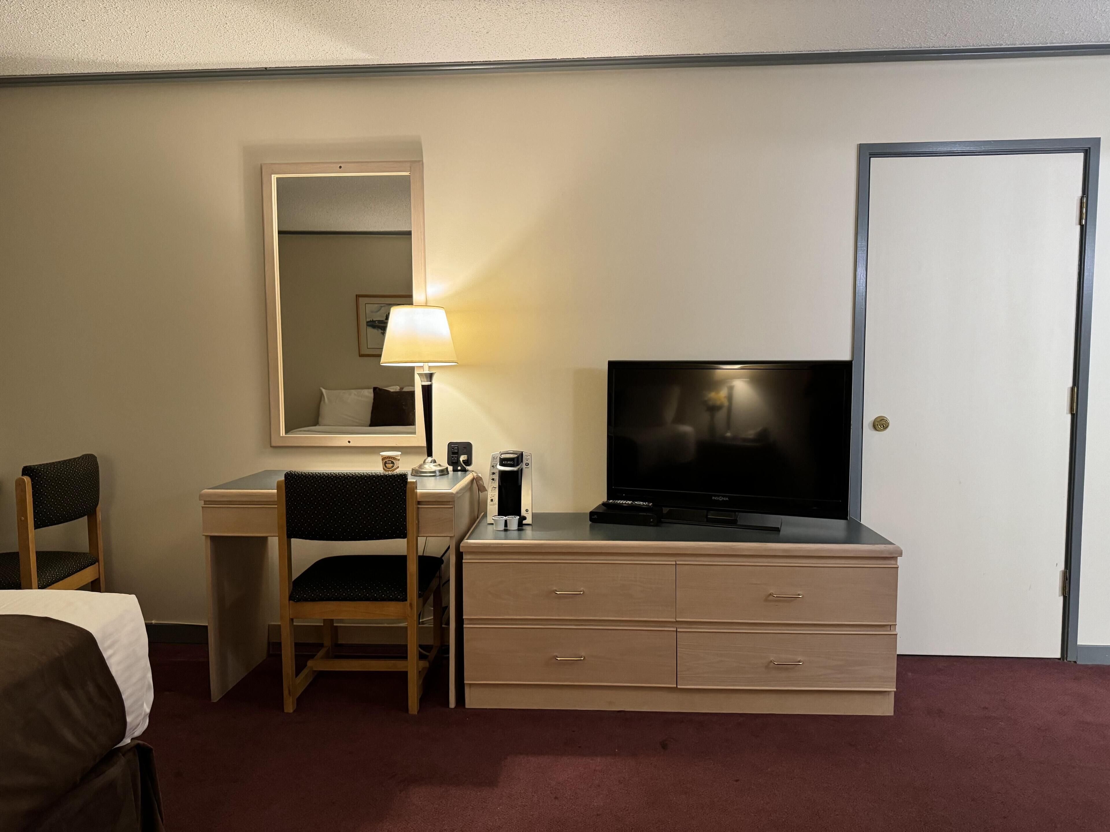 Una habitación de hotel con escritorio, silla, televisor y cómoda.
