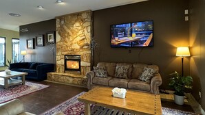 A living room with a stone fireplace, a television mounted on the wall, and a sofa with patterned cushions.