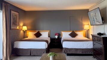 A hotel room with two beds, a wooden coffee table with a plant, a dresser, and a TV on the wall.