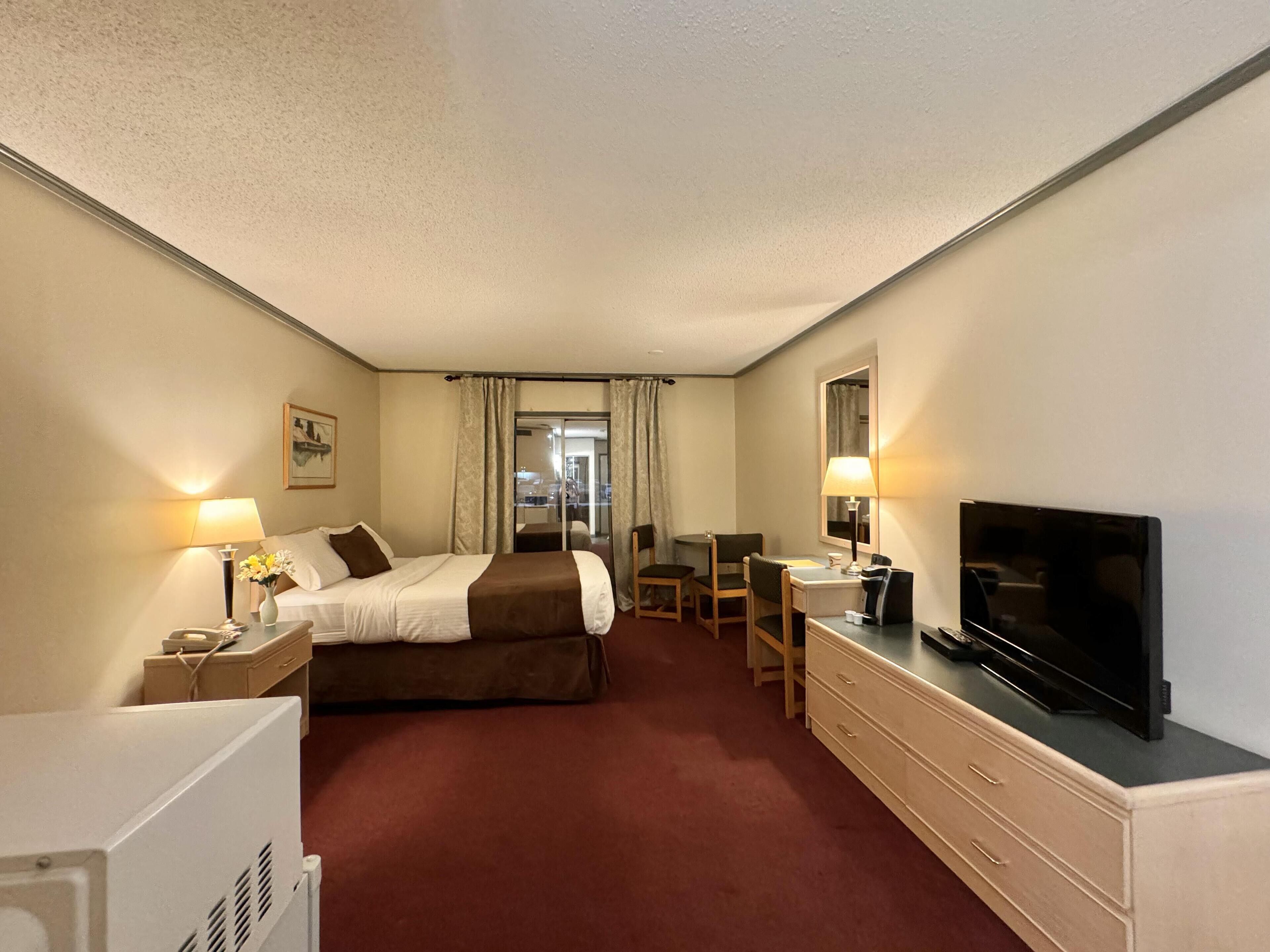 Ein Hotelzimmer mit einem Bett, einem Schreibtisch, einem Fernseher und Blick durch ein Fenster.