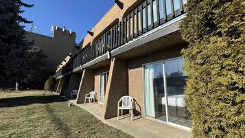 A building with a balcony, large windows, and a grassy courtyard.