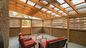 A covered outdoor seating area with wooden benches and a table, a ceiling fan, and a view of the outside.