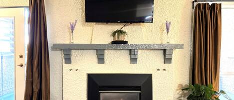 Una chimenea con un televisor montado encima, flanqueada por cortinas y plantas en macetas.