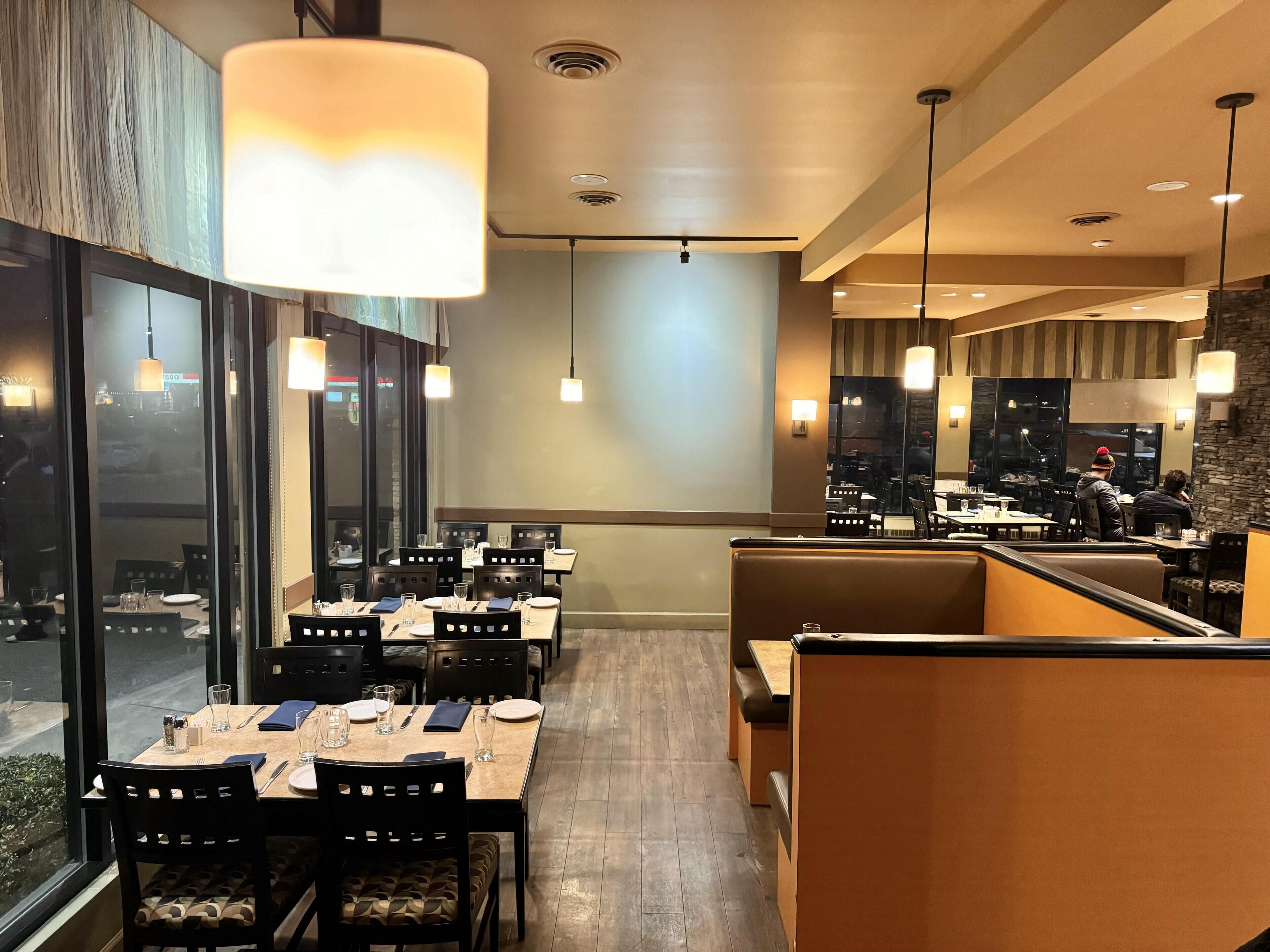 Um restaurante com mesas preparadas para refeições, um bar e vista da cidade através de grandes janelas.