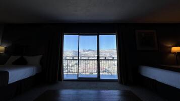 A hotel room with two beds, a large window with a view of snow-covered mountains, and a balcony.