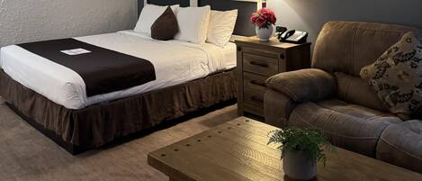 Una habitación de hotel con cama, mesita de noche, lámpara y sofá.