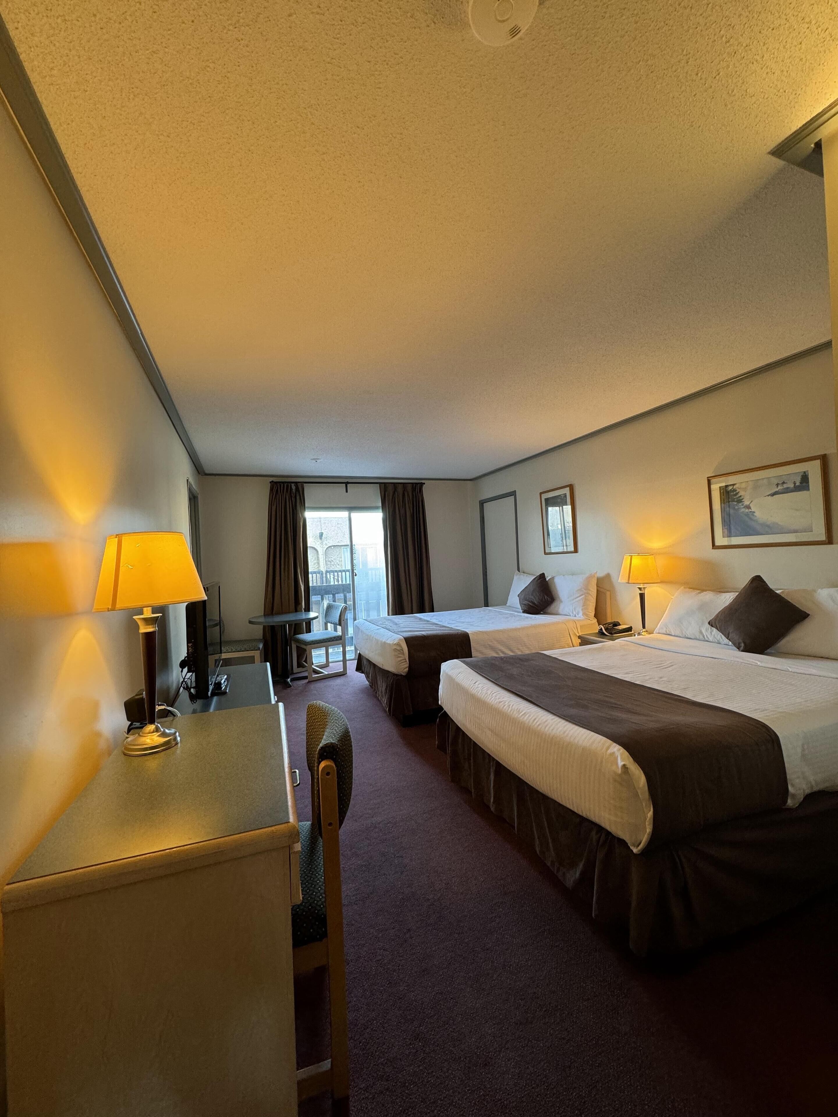 Een hotelkamer met twee bedden, een bureau, een stoel en een raam met gordijnen.
