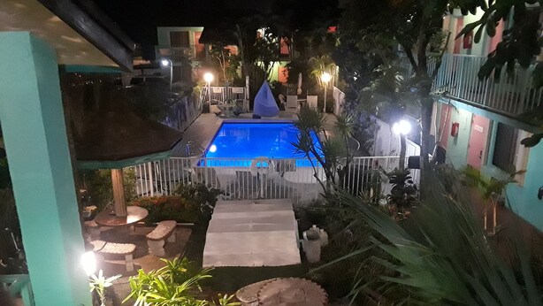 A nighttime view of a pool area with a clear pool, surrounded by a white fence, and various plants and outdoor furniture.