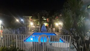 A swimming pool with a white fence, surrounded by potted plants and outdoor furniture.