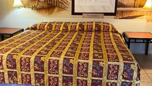 A bed with a patterned bedspread, two bedside tables, and wall art above the bed.