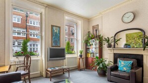 A living room with a fireplace, a bookshelf, a coffee table, and a comfortable seating area. - St Athans Hotel (London)