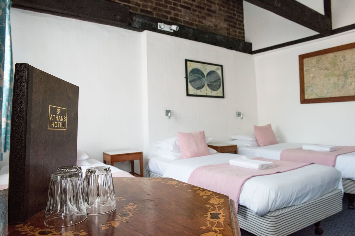 A hotel room with two beds, a wooden table with glasses, and a wall with a map and a framed picture.