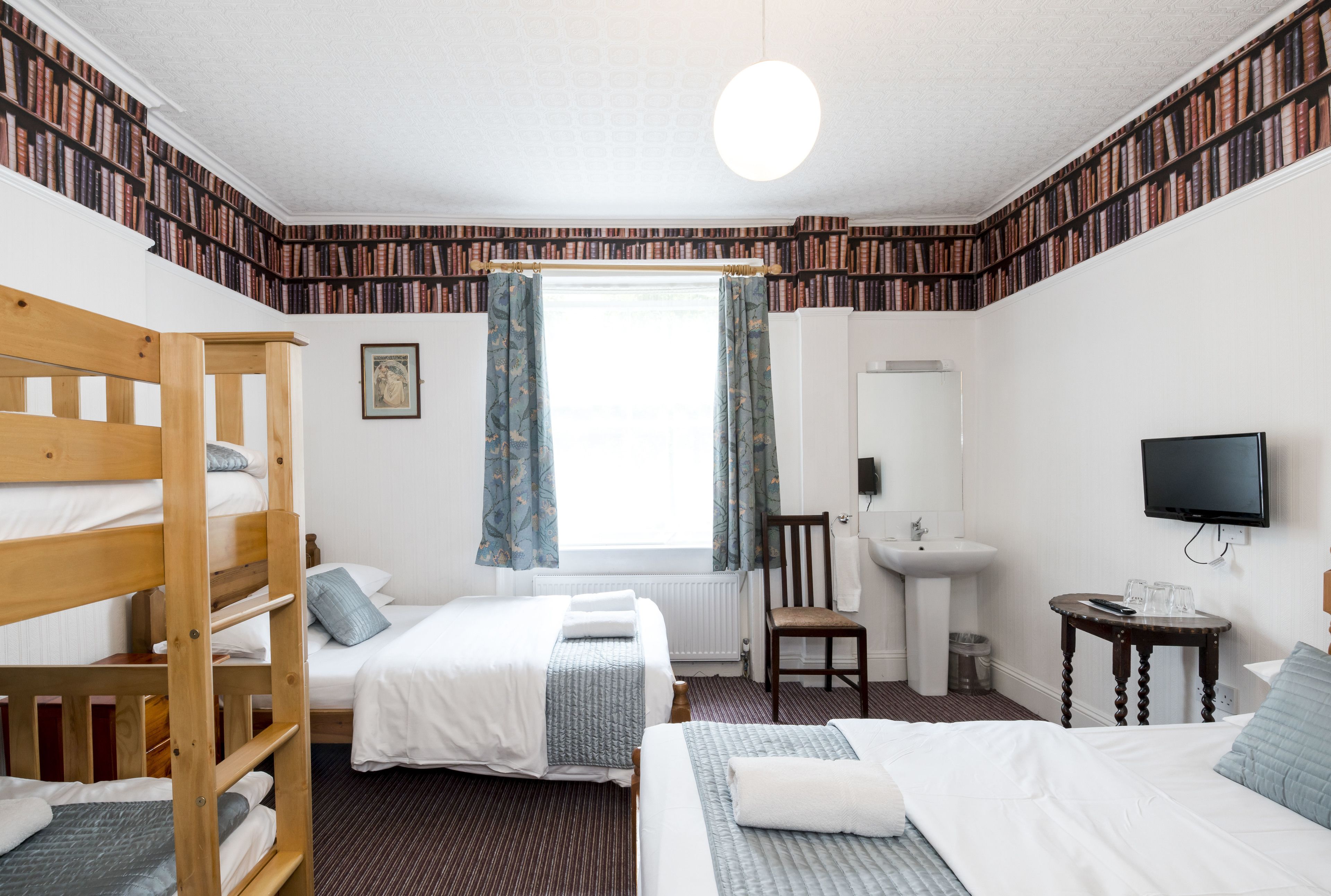 A hotel room with bunk beds, a desk, a chair, a sink, and a television.