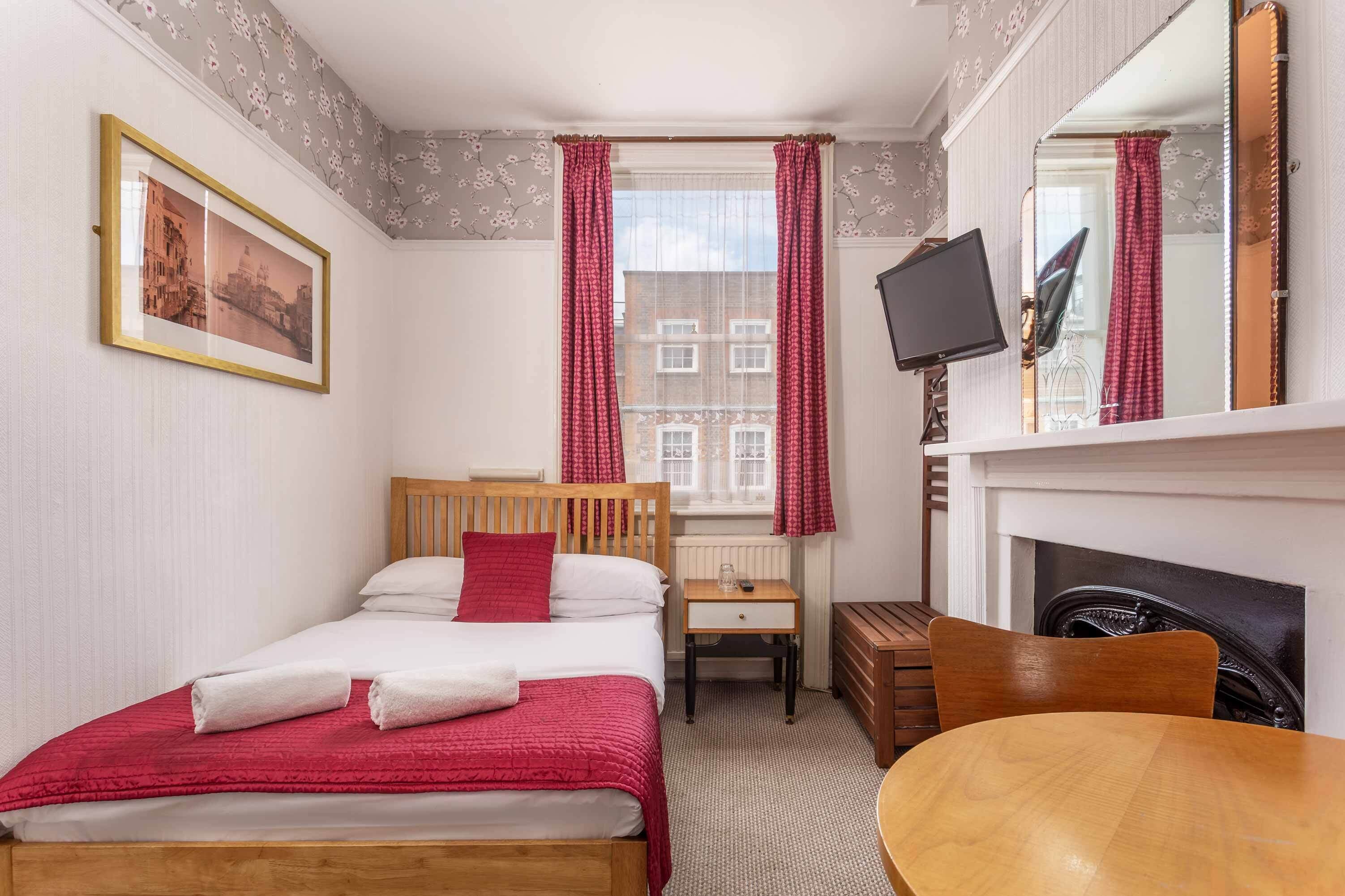 A hotel room with a bed, a desk, a chair, a TV, and a fireplace.