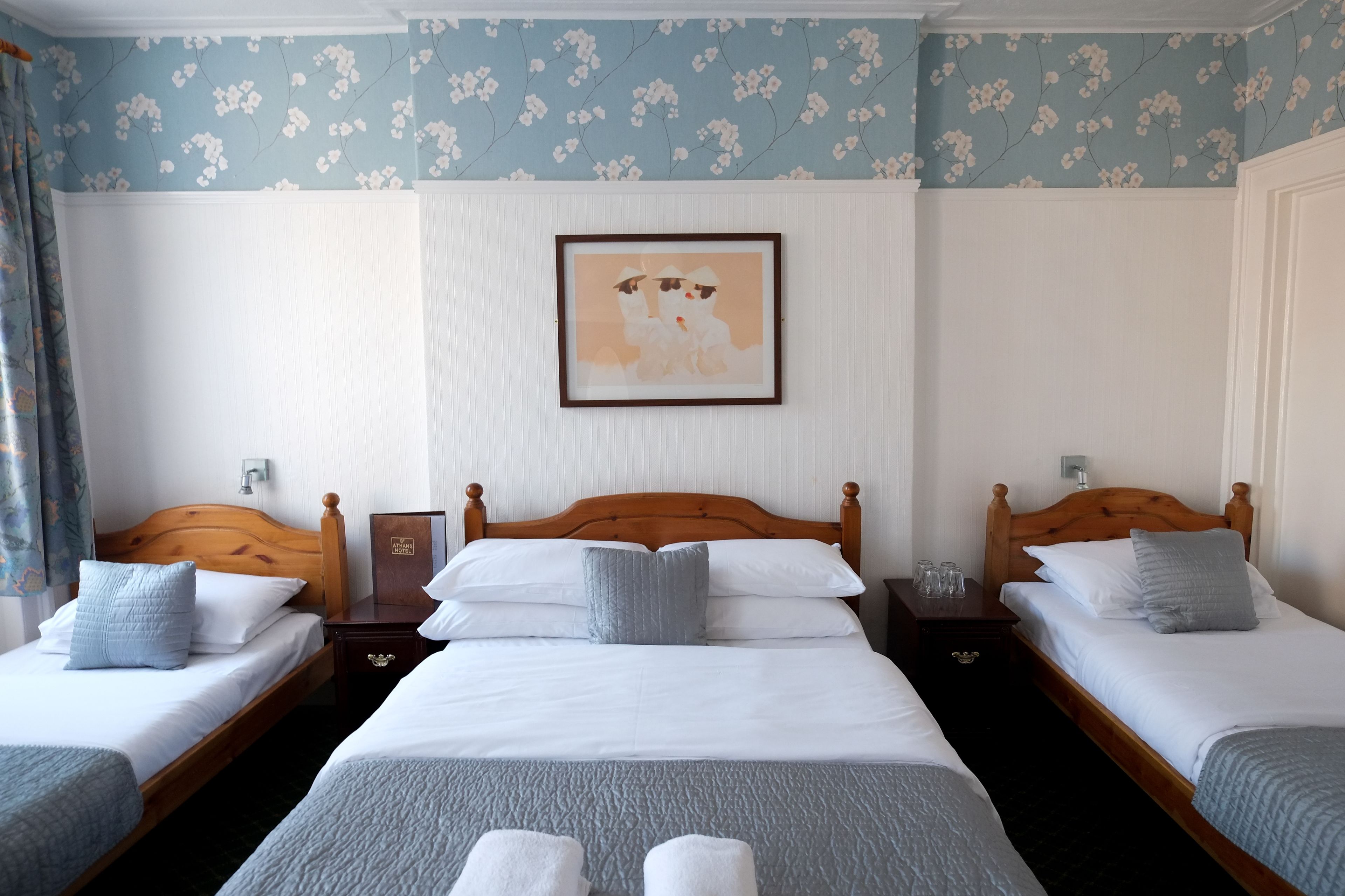 A hotel room with two single beds, a wooden headboard, white bedding, and a floral wallpaper design.
