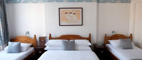 A hotel room with two single beds, a wooden headboard, white bedding, and a floral wallpaper design.