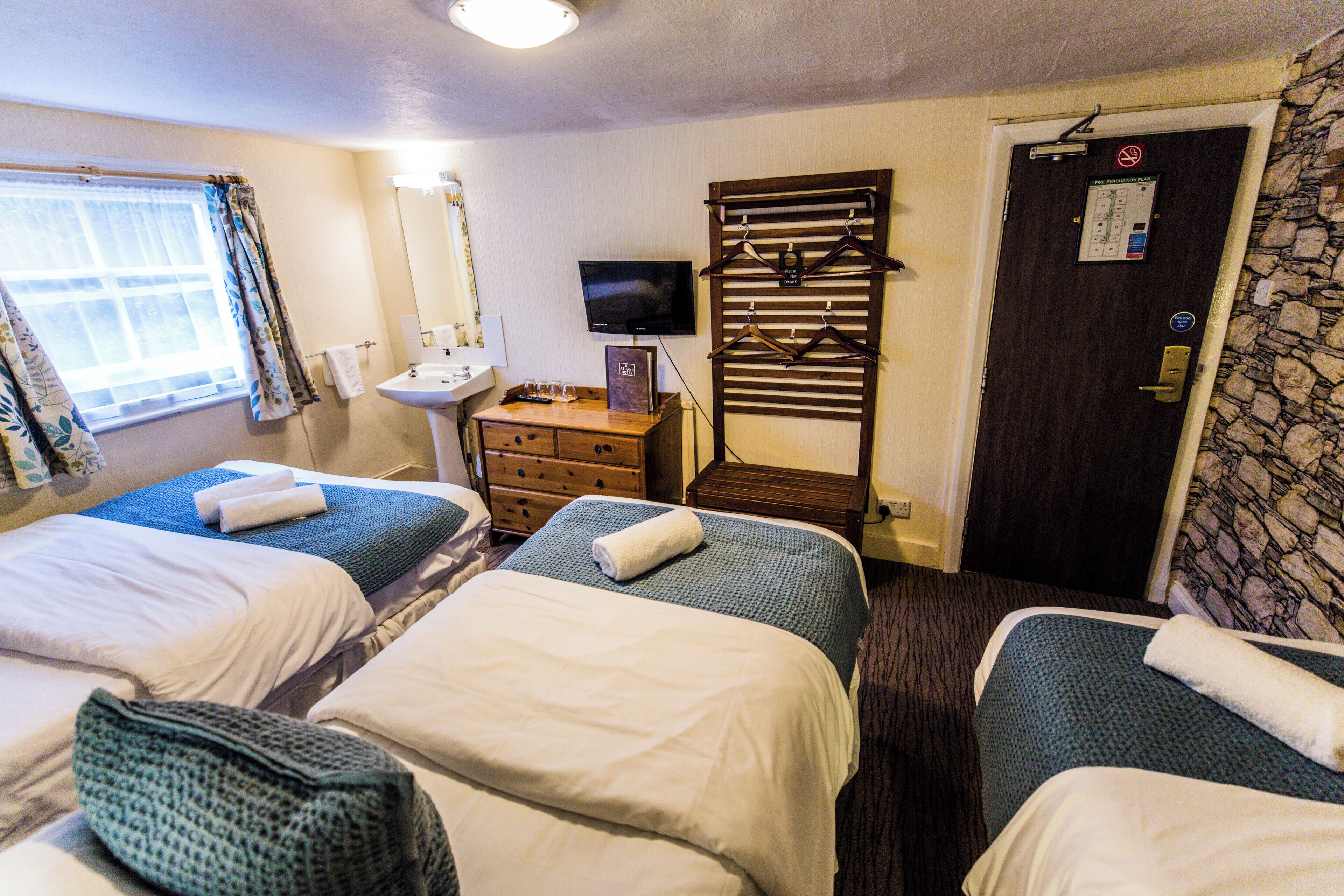 A hotel room with two beds, a sink, a television, and a door with a no-smoking sign.