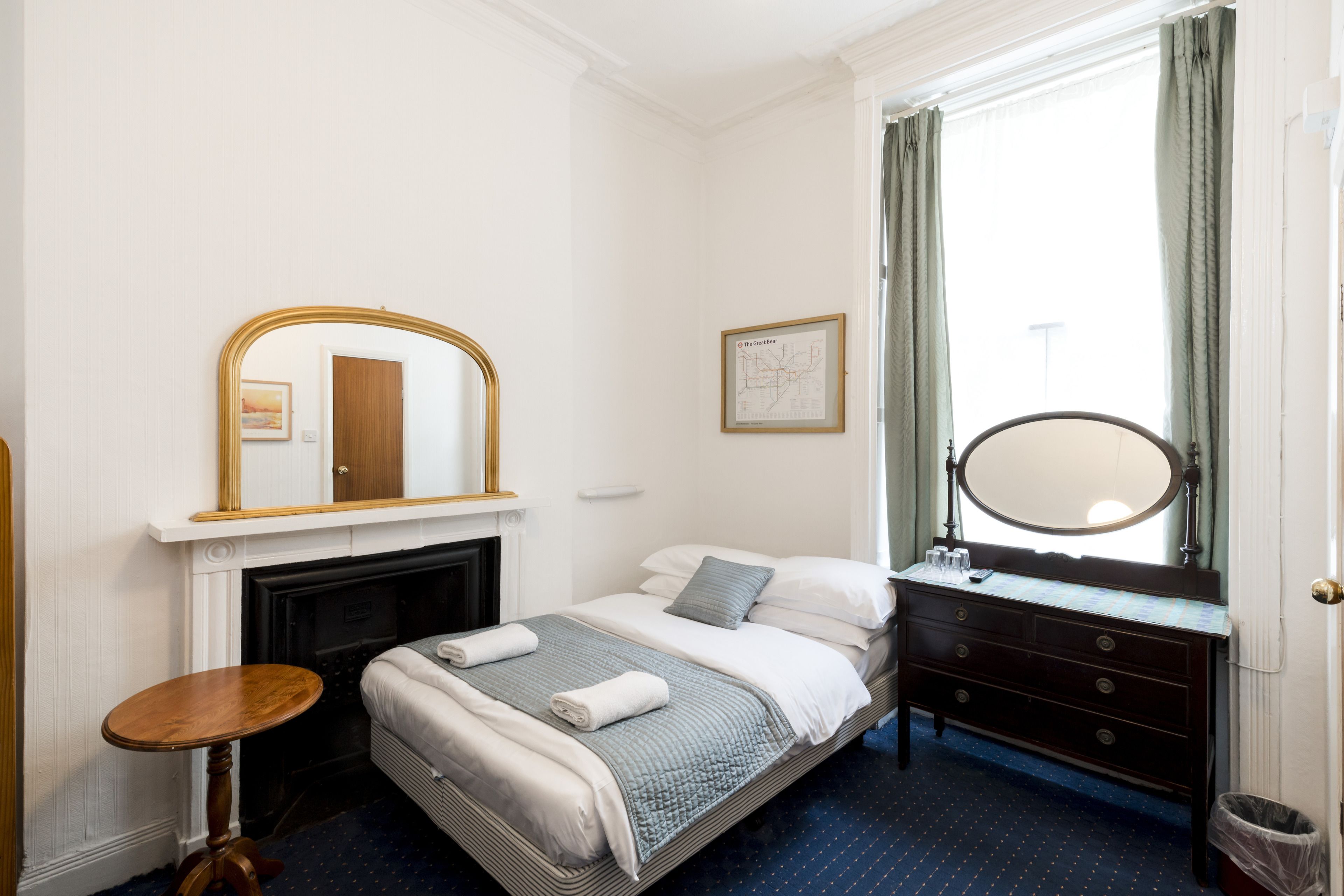 Ein Hotelzimmer mit einem Bett, einem Schminktisch, einem Spiegel, einem kleinen Tisch und einem Kamin.