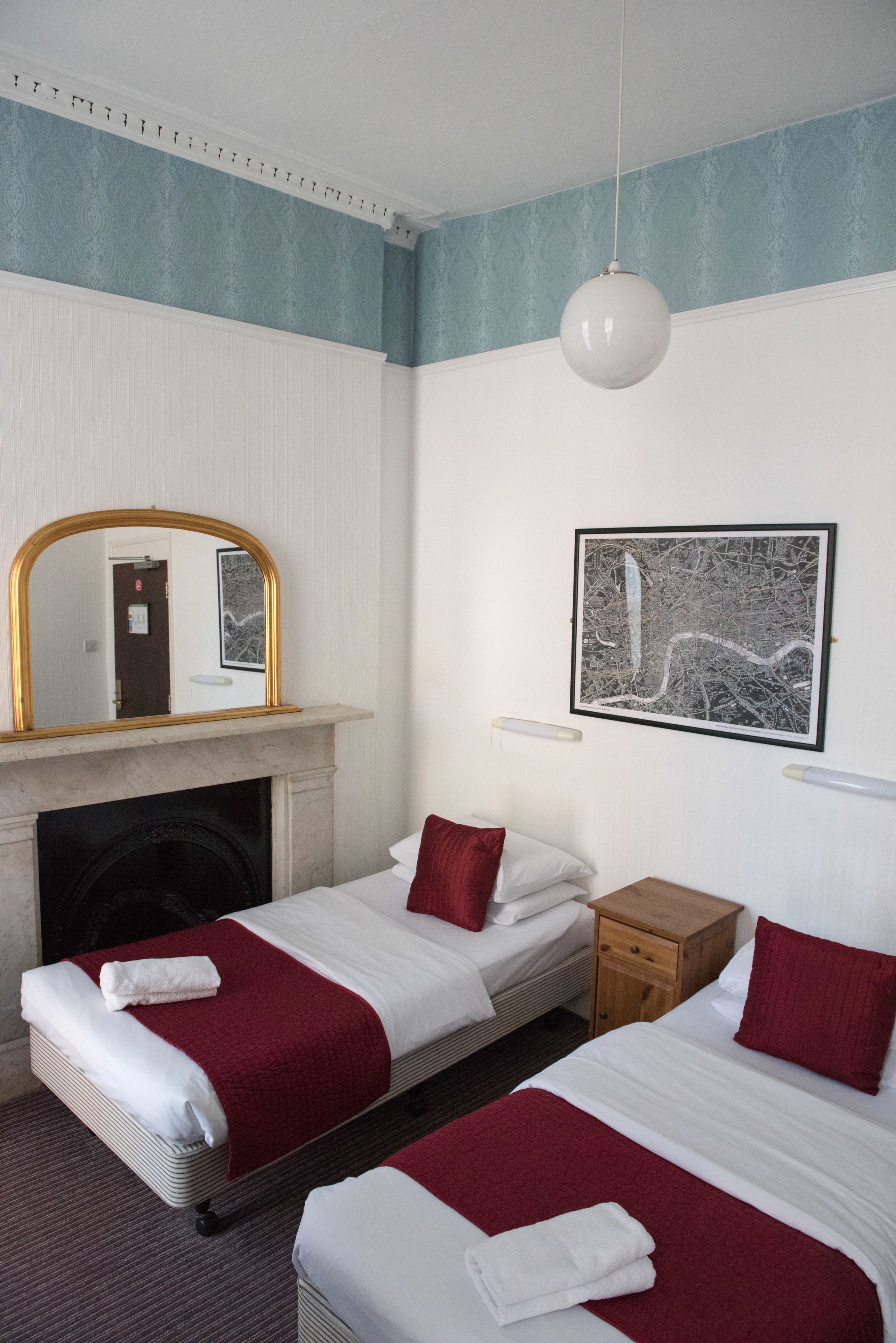 A hotel room with two beds, a fireplace, a mirror, and a framed picture on the wall.
