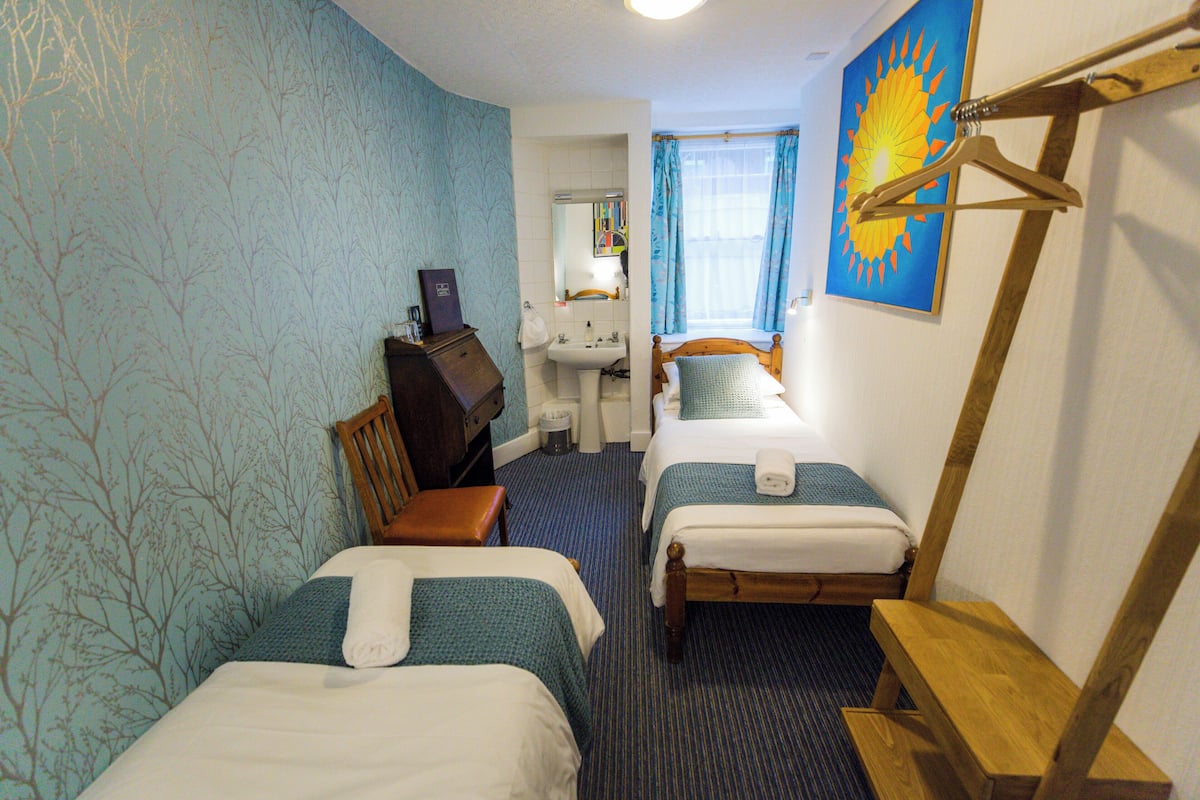 A hotel room with two beds, a desk, a chair, a sink, and a window with curtains.