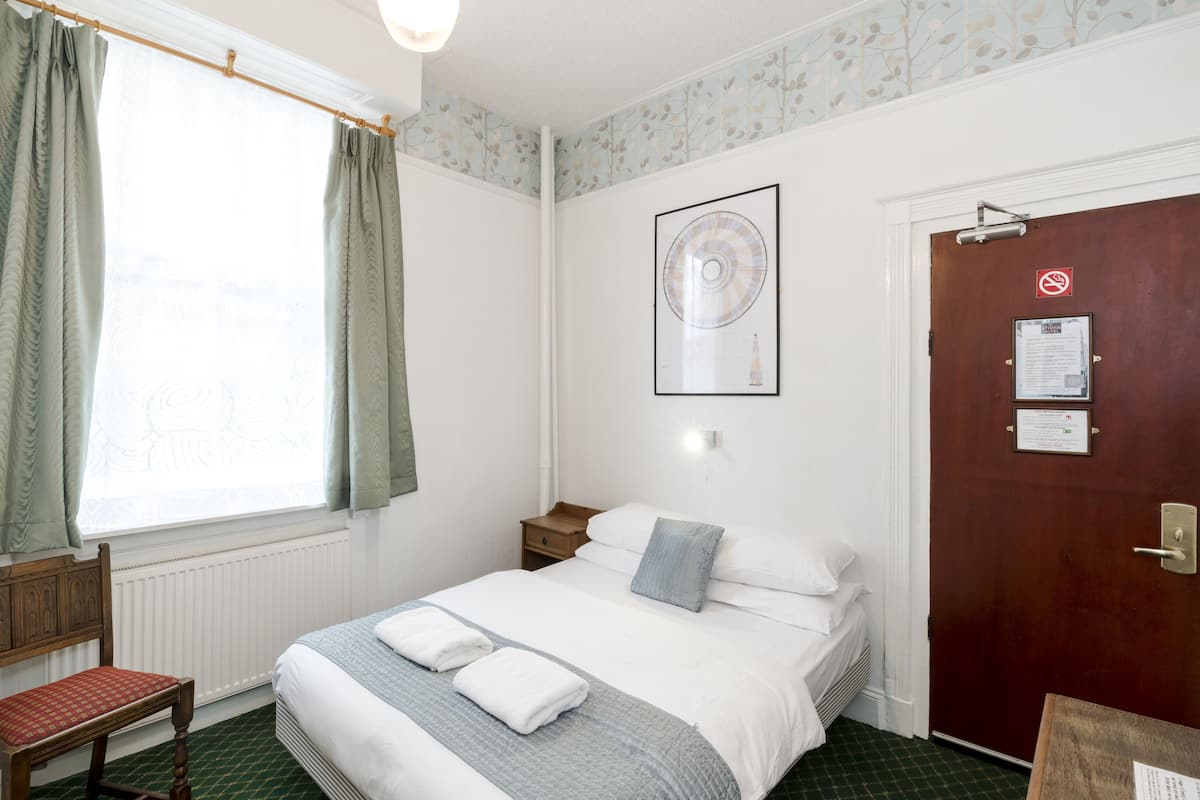 A hotel room with a bed, a chair, a wooden door, and a window with curtains.