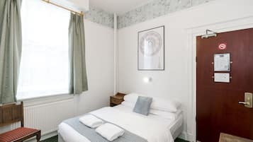 Une chambre d’hôtel avec un lit, une chaise, une porte en bois et une fenêtre avec des rideaux.