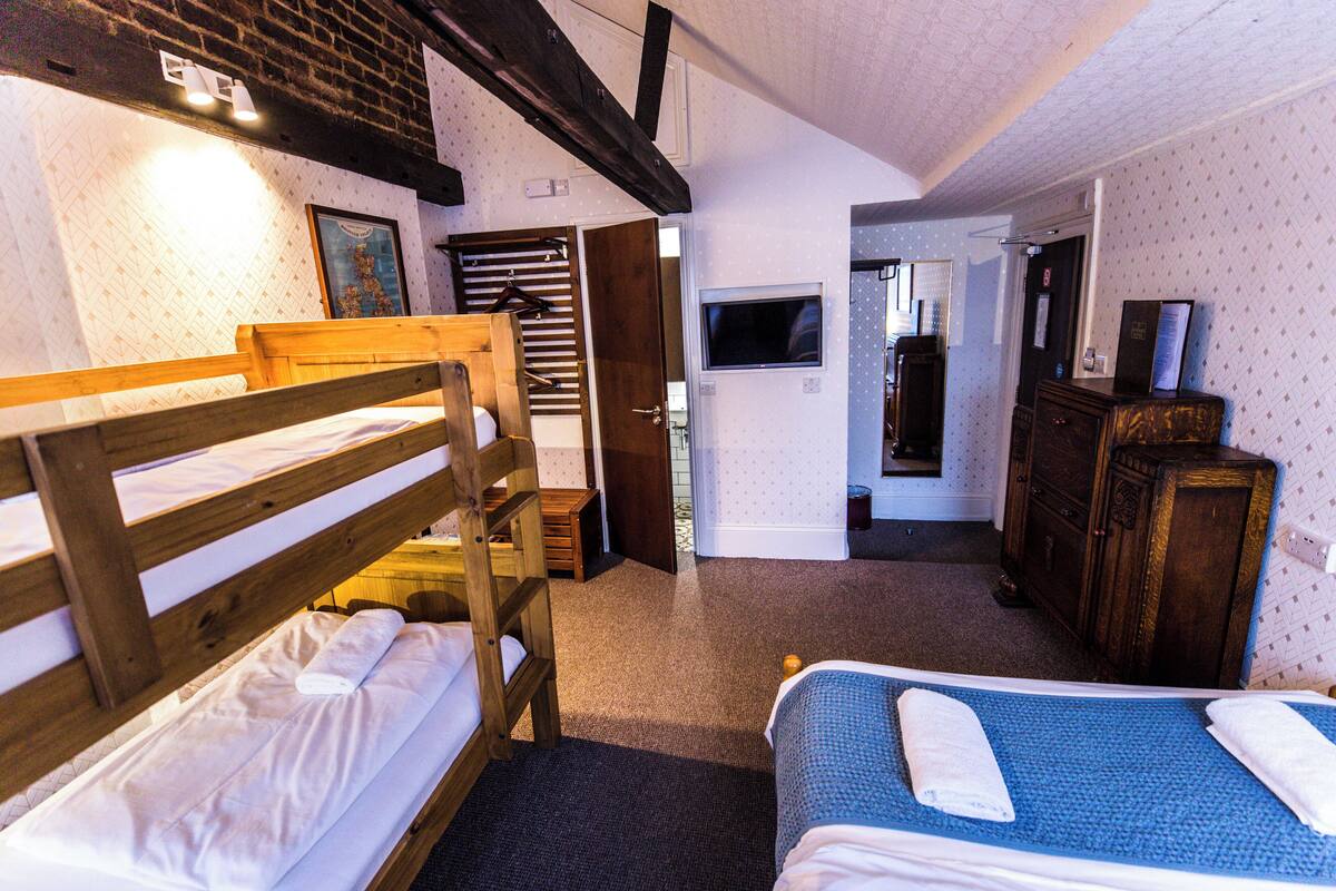 A room with two bunk beds, a wooden dresser, a television, and a door leading to another room.