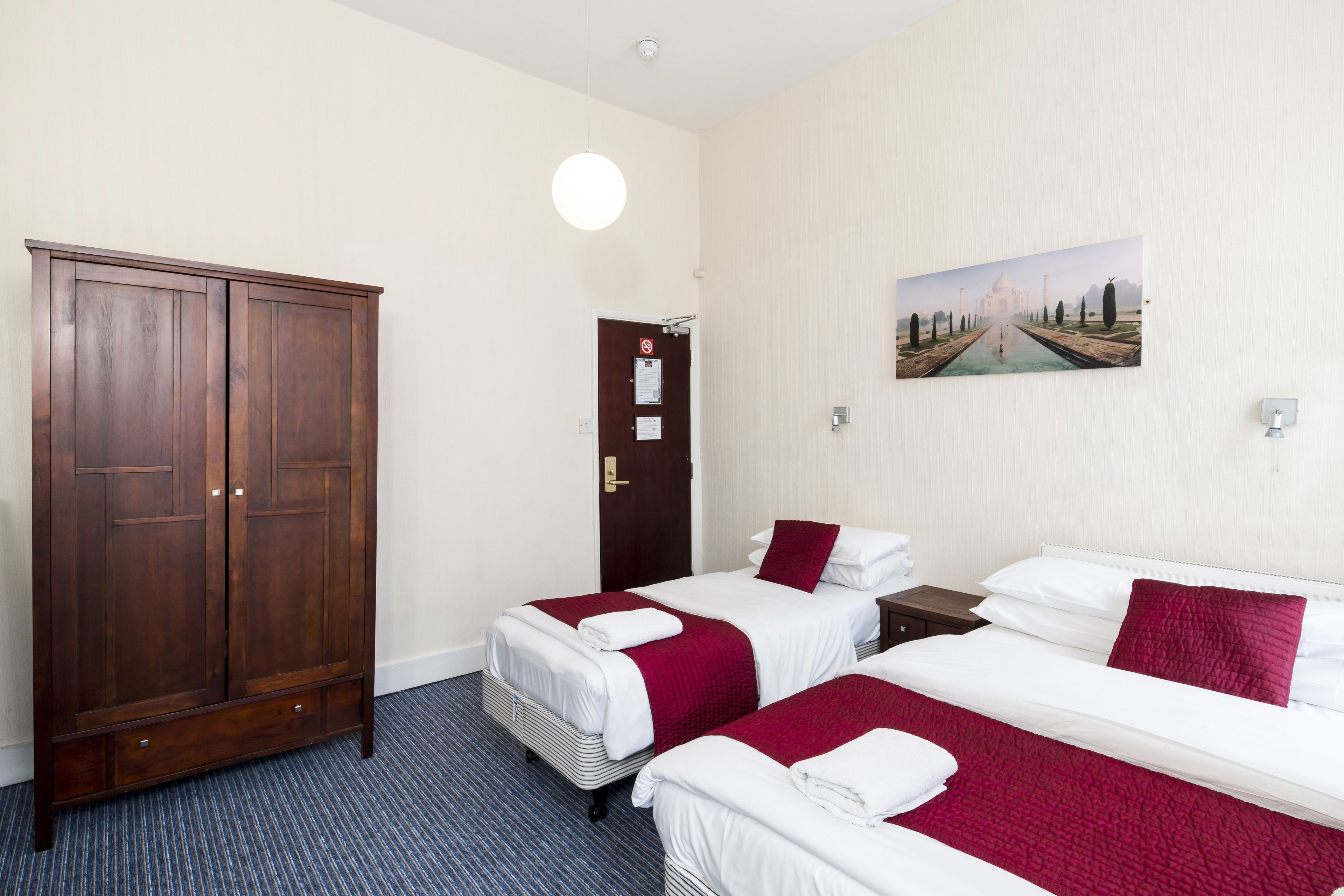 Una habitación de hotel con dos camas, un armario, una puerta con un letrero y un cuadro en la pared.