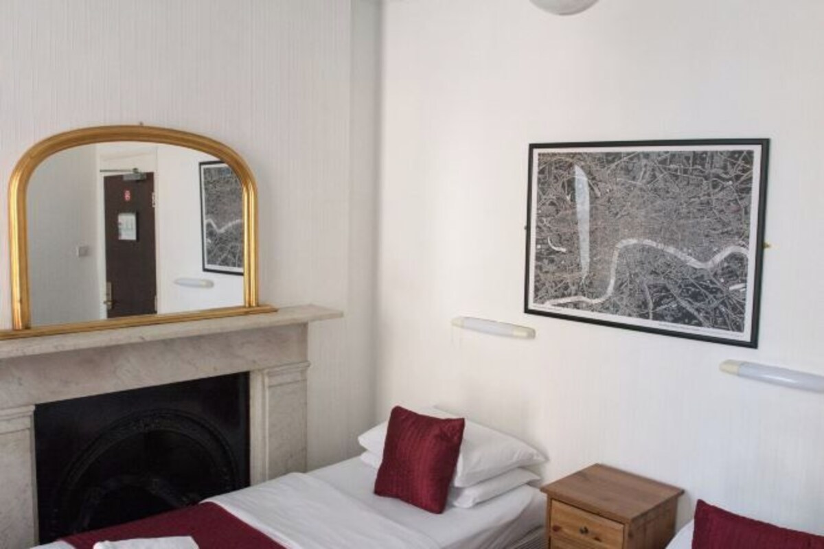 A bedroom with a bed, a nightstand, a mirror, a fireplace, and a framed picture on the wall.