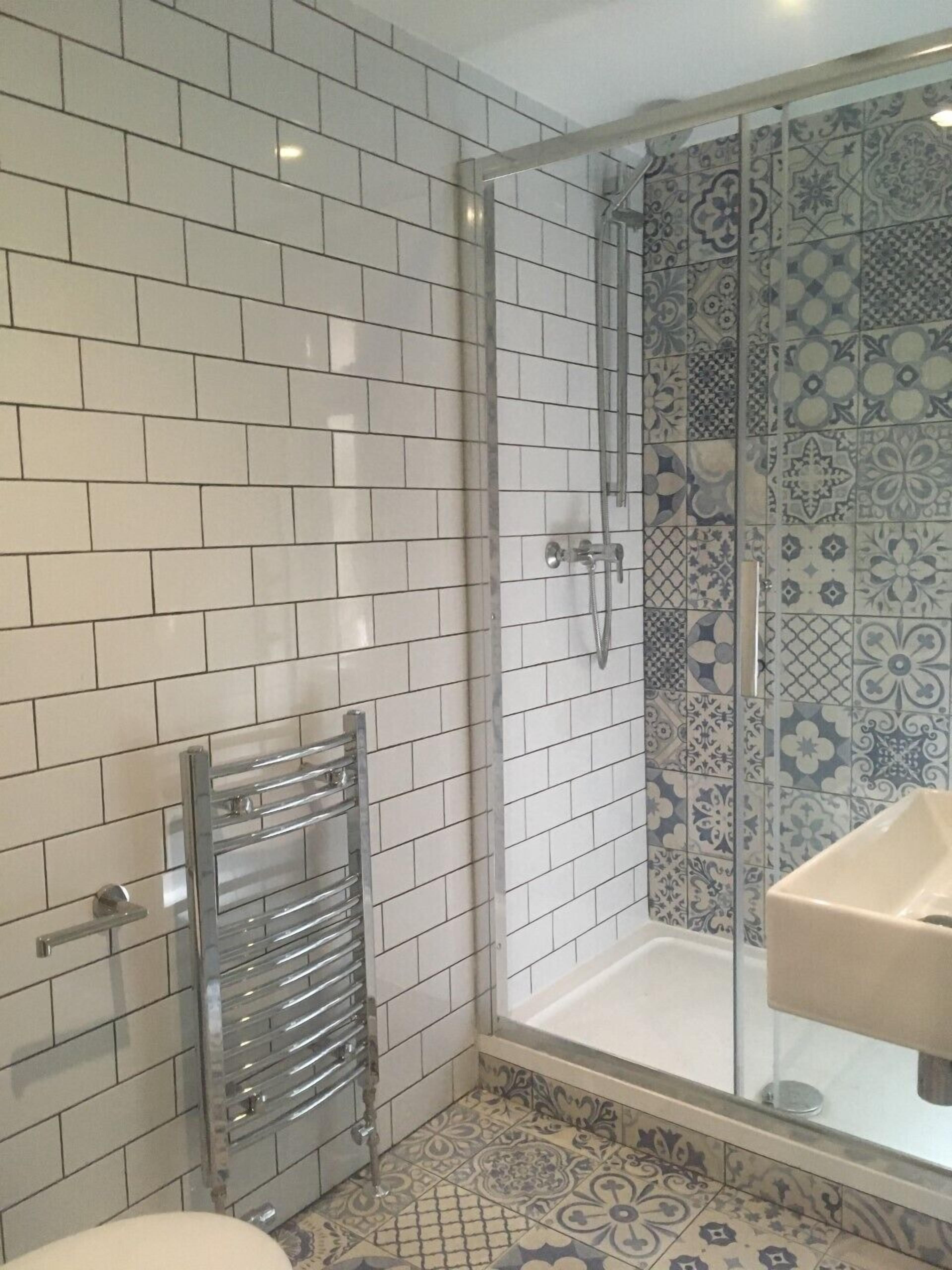 A bathroom with white subway tiles, a glass shower enclosure, and a sink with a patterned backsplash.