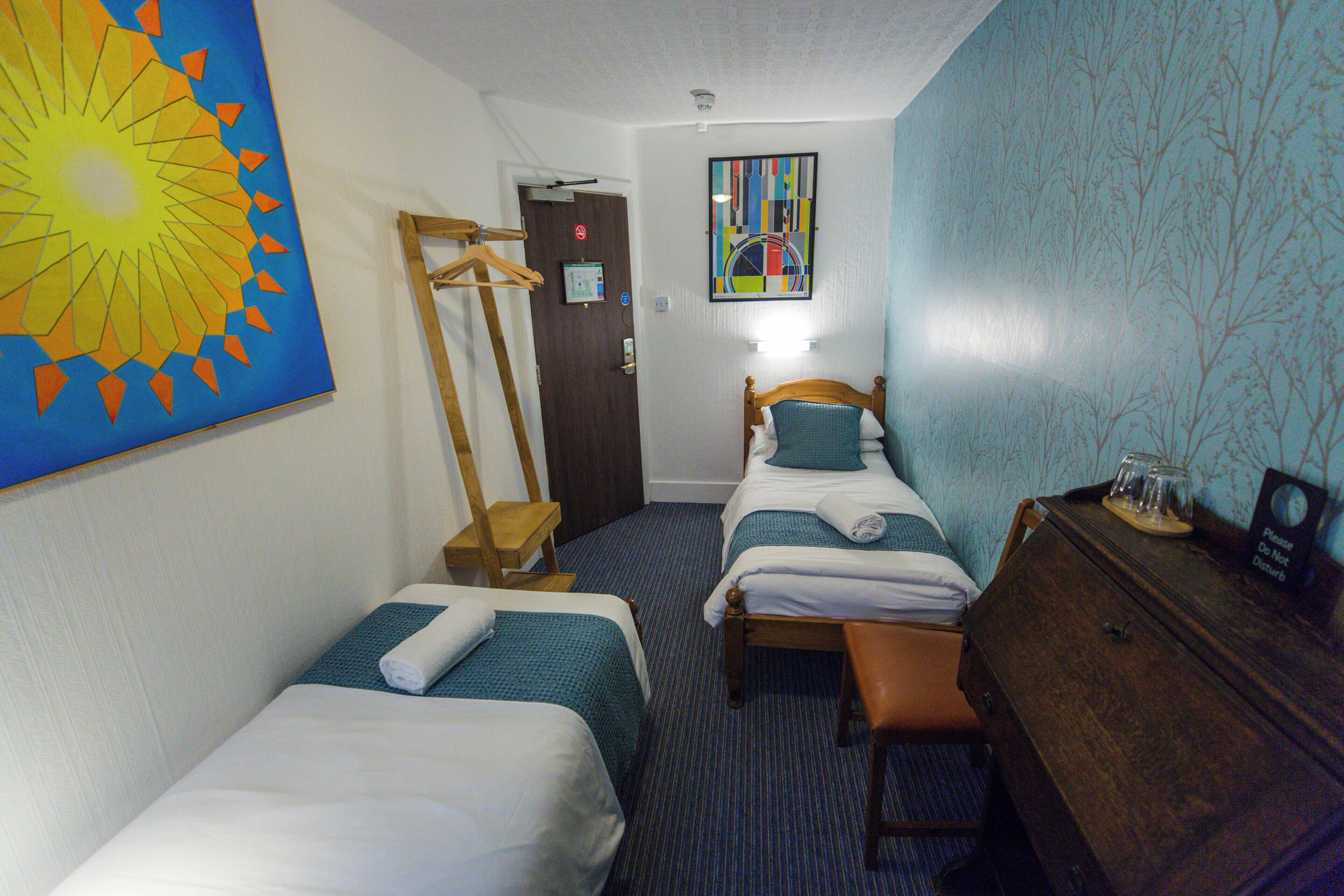 A hotel room with two beds, a wooden dresser, a desk, and a painting on the wall.