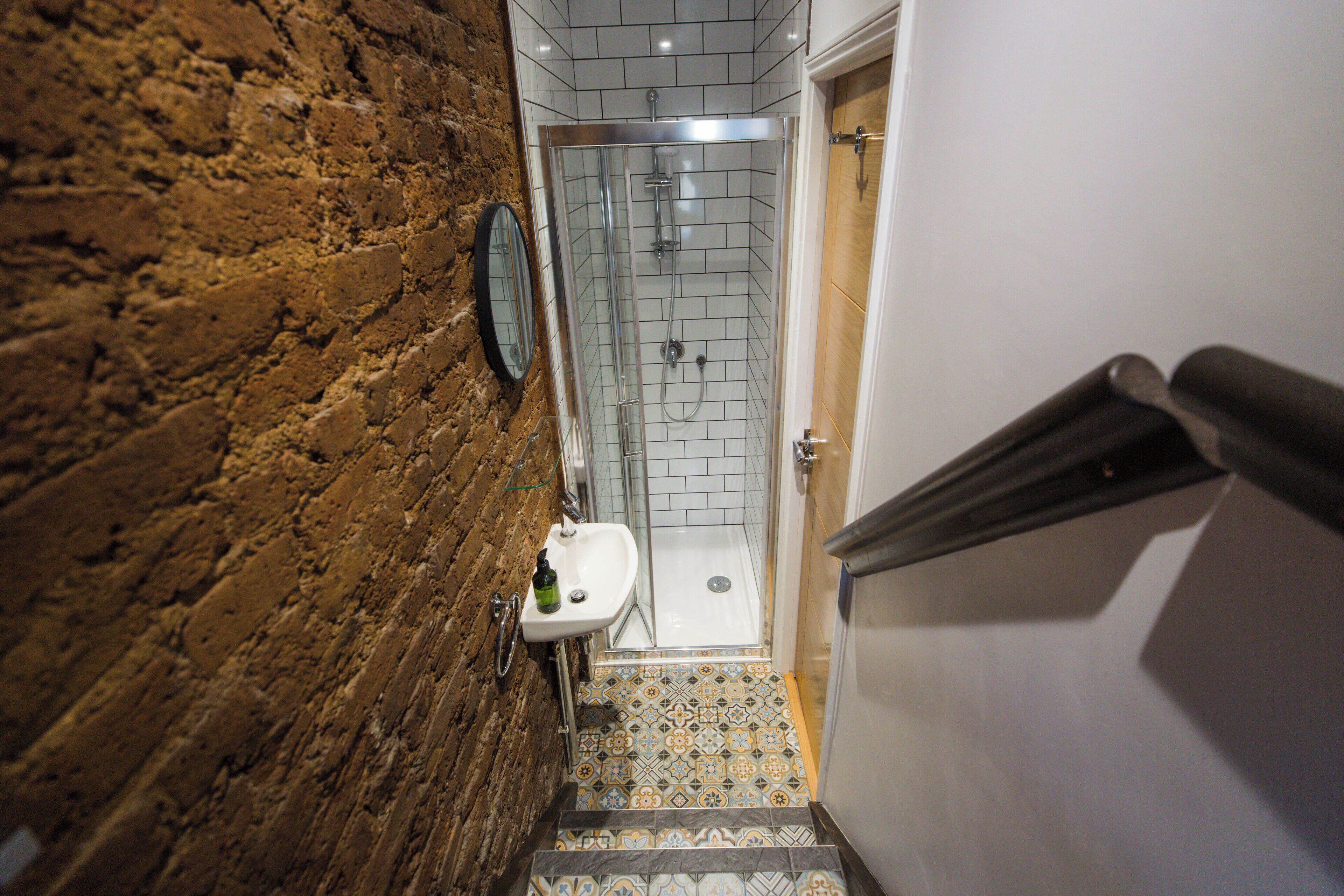A narrow hallway with a shower area, a sink, and a mirror.