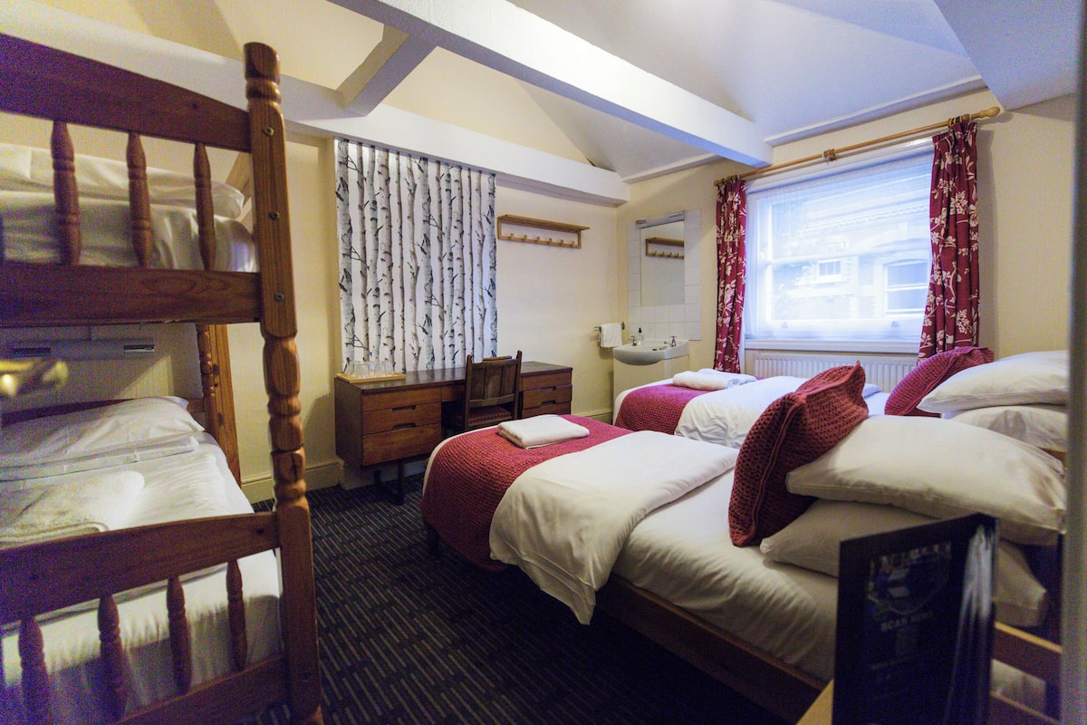 A hotel room with bunk beds, a desk, a chair, a window with curtains, and a mirror.