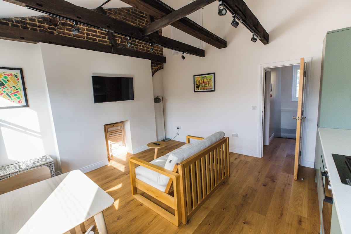 A room with a wooden bench, a small table, a TV mounted on the wall, and a door leading to another room.