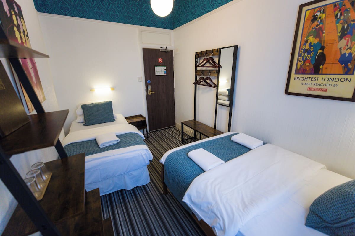 A hotel room with two beds, a desk, a mirror, and a poster on the wall.