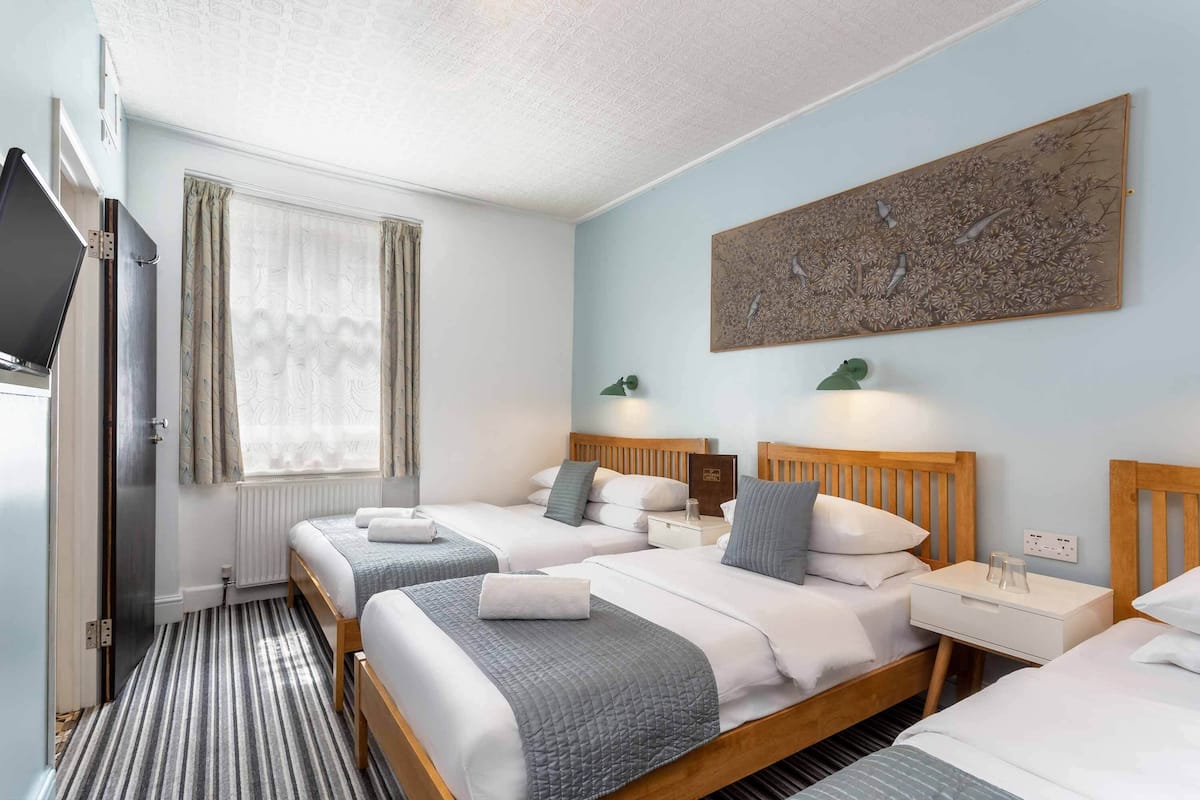 A hotel room with two beds, a large artwork on the wall, and a window with curtains.