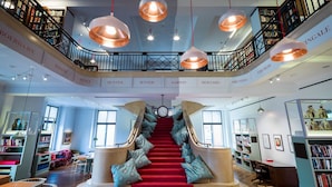 A library with a red carpet staircase, bookshelves, and hanging copper pendant lights. - St Athans Hotel (London)