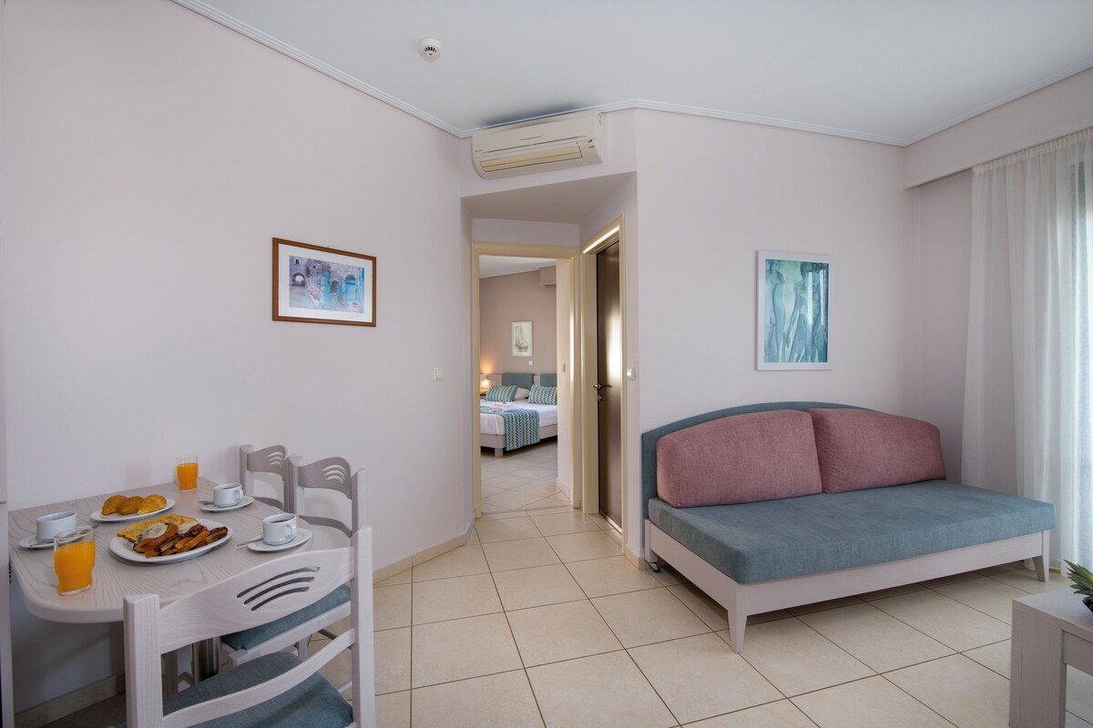 Quarto de hotel moderno com área de refeições, sofá e cama.