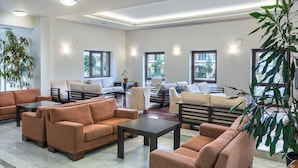 A spacious living area with multiple sofas and armchairs, a coffee table, and large windows providing natural light. - Creta Palm Hotel (Chania)