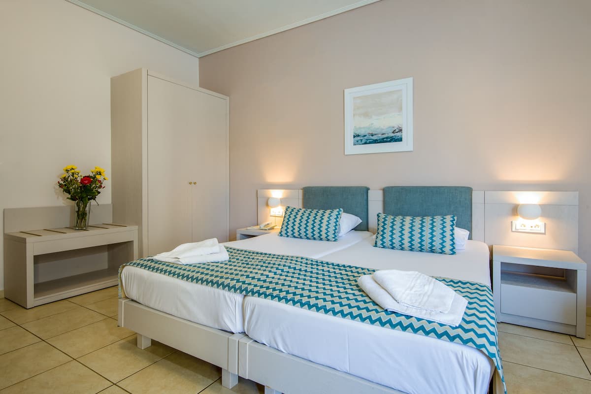 A neatly arranged hotel room with a large bed, two bedside tables, a nightstand, a wardrobe, and a wall-mounted picture.